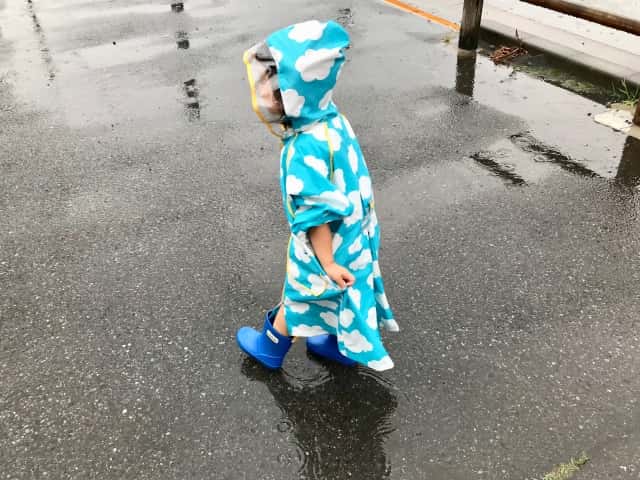 雨の中、空色のレインコートを着る子供